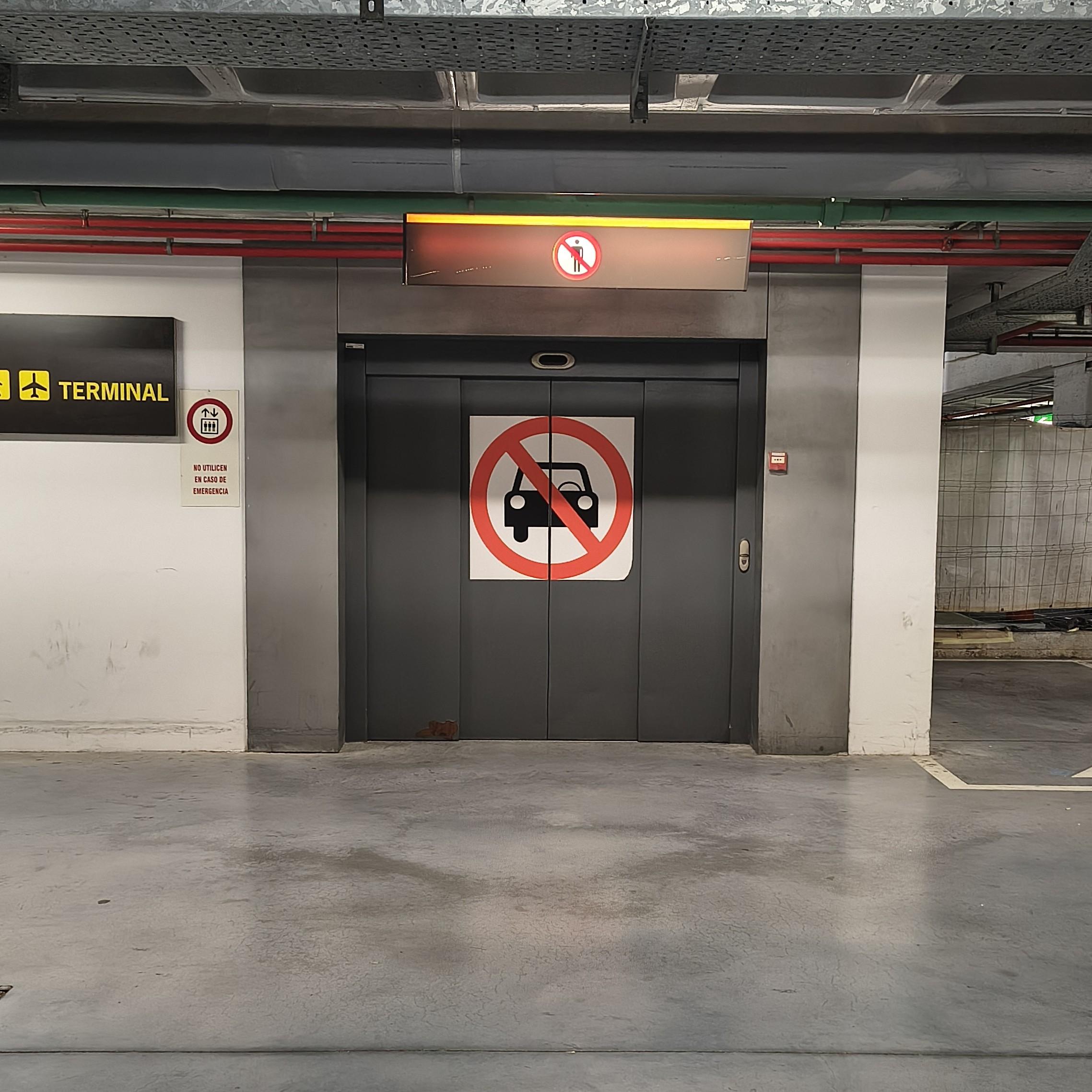 Garaje del aeropuerto. Puerta amplia de ascensor con un signo MUY GRANDE de prohibido automóviles.