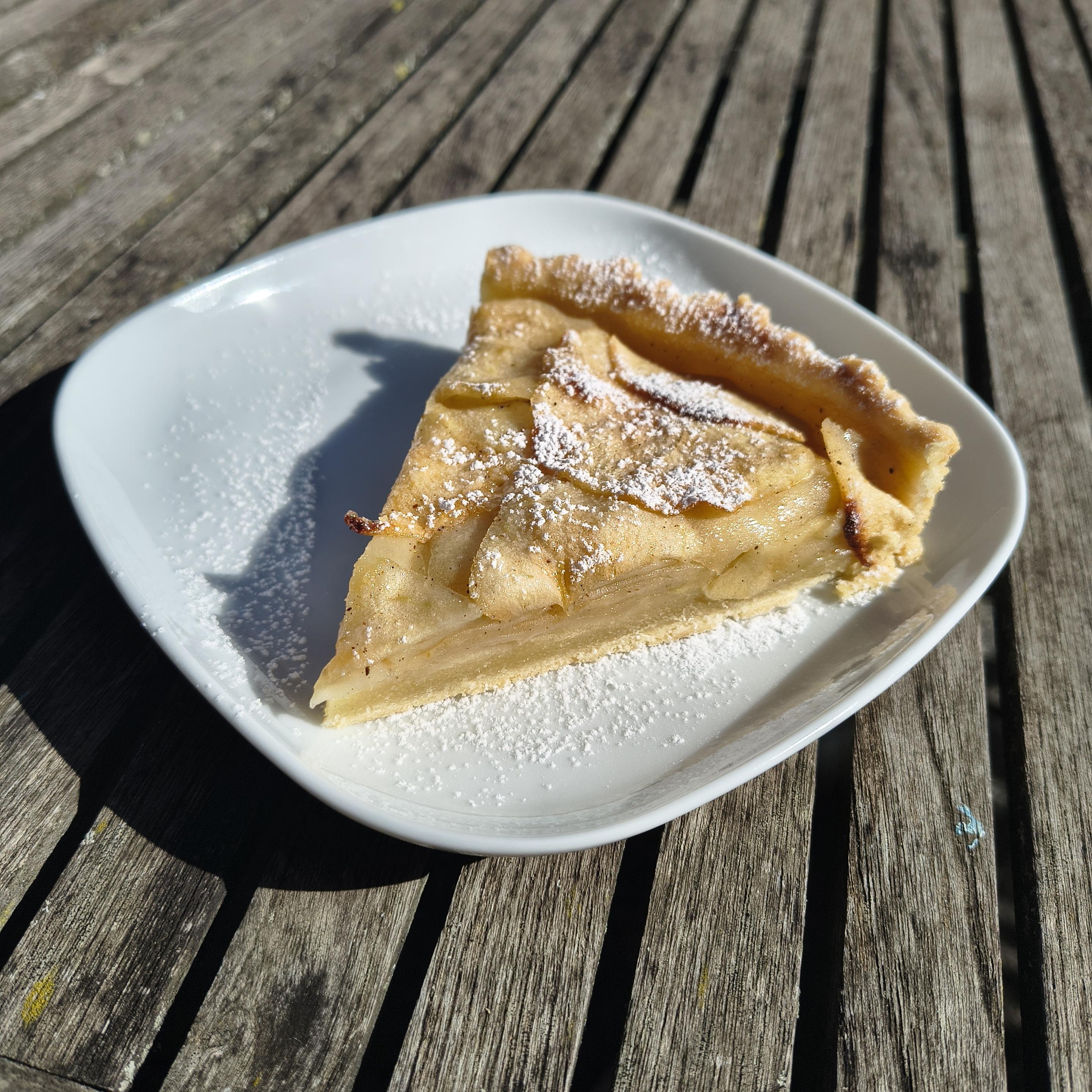 Trozo de tarta de manzana en un plato. Tiene una masa abajo y encima, muchas rodajas muy finas. Está espolvoreada con azúcar glasé.